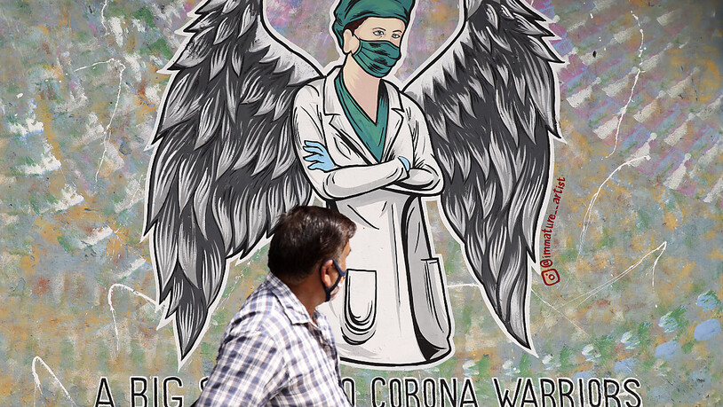 Ein Mann geht in Neu-Delhi  an einem Wandgemälde vorbei, das einen Mitarbeiter im Gesundheitswesen mit Flügeln zeigt. Indien hat heute einen neuen Tageshöchstwert an Todesfällen im Zusammenhang mit dem Coronavirus gemeldet. Foto: Amit Sharma/AP/dpa