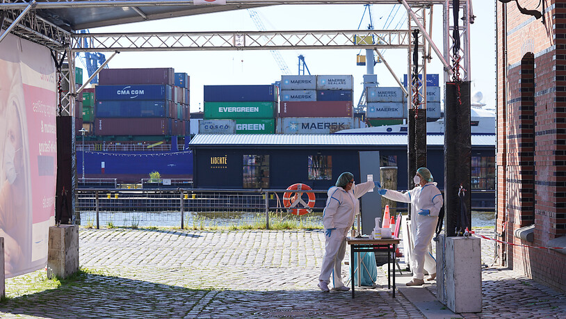 Eine Mitarbeiterin einer Corona-Schnelltest Drive-in-Station im Hafen überreicht einer Kollegin eine Testprobe. Foto: Marcus Brandt/dpa