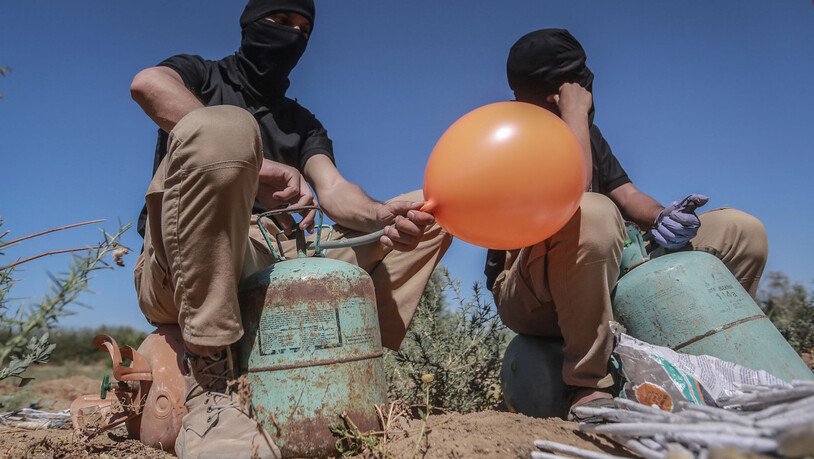 Maskierte Palästinenser füllen in einem Gebiet östlich von Gaza-Stadt Ballons mit Kühlgas, die dann mit Brandsätzen und brennbarem Material versehen werden und vom Wind in israelisches Gebiet getragen werden sollen. Foto: Mohammed Talatene/dpa Foto:…