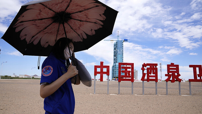 Ein Arbeiter hält einen Regenschirm in der Nähe des Raumschiffs Shenzhou-12, das auf der Startrampe mit den chinesischen Schriftzeichen "China Jiuquan Satellite Launch Center" steht. Foto: Ng Han Guan/AP/dpa