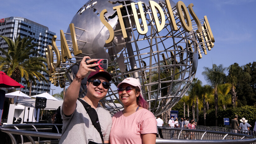 Ein Paar fotografiert sich vor dem Schriftzug Universal Studios Hollywood auf einer Weltkugel-Skulptur. Am Dienstag hob Kalifornien die meisten seiner COVID-19-Beschränkungen auf und läutete das ein, was als die "Große Wiedereröffnung" des Staates…