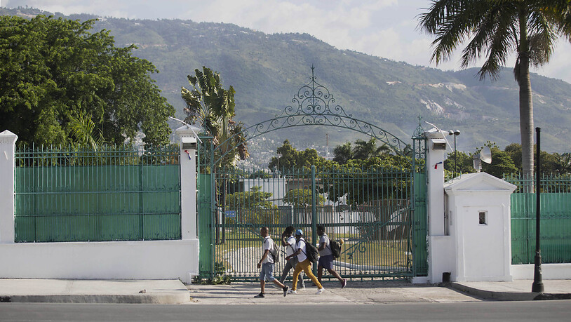 Fußgänger gehen am Tor des Präsidentenpalast vorbei. Präsident Moise war in der Nacht zum Mittwoch gegen 1.00 Uhr (Ortszeit) in seiner Residenz erschossen worden. Trotz erster Festnahmen ist die Lage in Haiti weiterhin angespannt. Foto: Joseph Odelyn/AP…