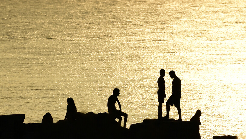 Menschen stehen auf Felsen in der Nähe eines Strandes im Vorort Kavouri. Die extreme Hitzewelle in Griechenland lässt nicht locker. Seit über einer Woche klettern die Temperaturen für mehrere Stunden täglich auf über 40 Grad. Foto: Michael Varaklas/AP/dpa