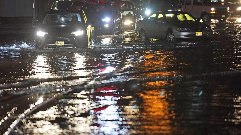 Autos bahnen sich ihren Weg durch New Jersay über überflutete Straßen und an verlassenen Autos vorbei. Foto: Seth Wenig/AP/dpa