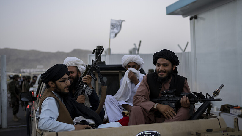 Taliban-Kämpfer sitzen auf der Ladefläche eines Autos auf dem Gelände des Flughafens in Kabul und halten Waffen in ihren Händen. Foto: Bernat Armangue/AP/dpa