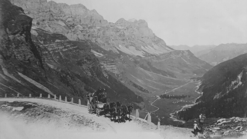 Postkartensujet aus dem Jahr 1921: Die Reisenden in der Postkutsche geniessen von der Klausenpassstrasse aus den Ausblick auf den Urnerboden, der grössten Alp der Schweiz. Auf dem Kutscherbock sitzen der Postillon und der Kondukteur.