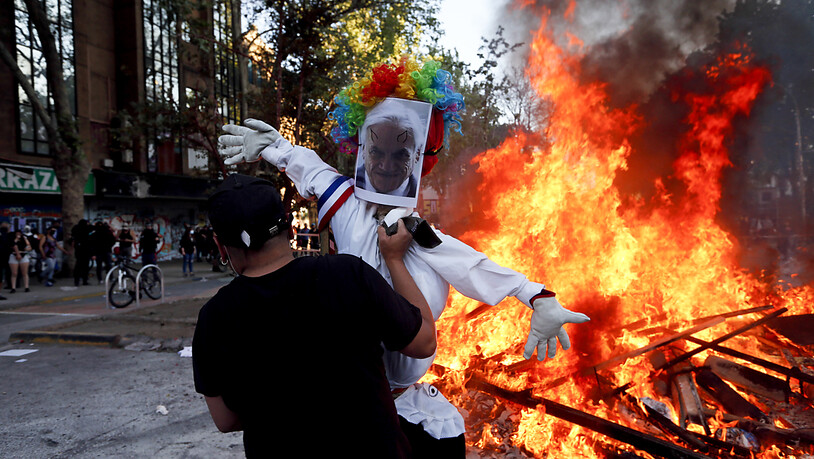 Ein Demonstrant hält ein Puppe mit einem Foto des chilenischen Präsidenten Pinera bei einem Feuer. Foto: Luis Hidalgo/AP/dpa