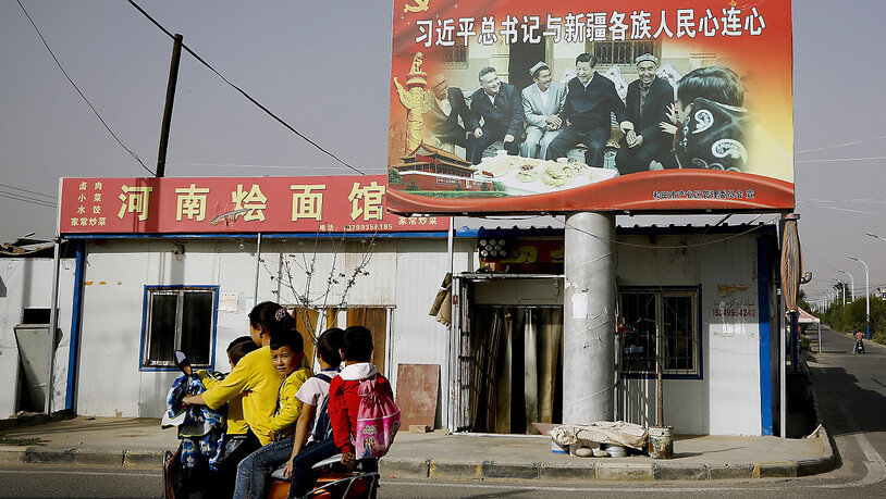 ARCHIV - Eine uigurische Frau fährt mit Schulkindern an einem Bild von Chinas Präsident Xi Jinping und einer Gruppe von uigurischen Ältesten vorbei. 43 Nationen haben am Donnerstag in einer UN-Vollversammlung Menschenrechtsverletzungen Chinas unter…