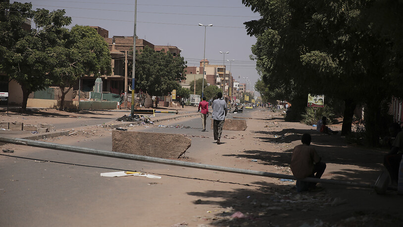 Personen gehen auf einer Straße, auf der Steine als behelfsmäßigen Barrikade liegen. Foto: Marwan Ali/AP/dpa