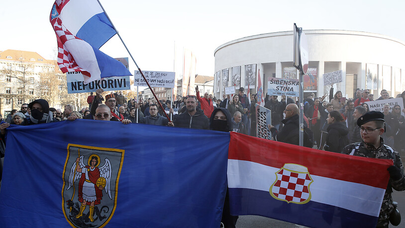 Menschen stehen während eines Protestes mit Fahnen und Plakaten auf der Straße. Am Samstag sind in der kroatischen Hauptstadt Zagreb Tausende Menschen durch die Straßen gezogen, um gegen die Corona-Maßnahmen der kroatischen Regierung zu protestieren…