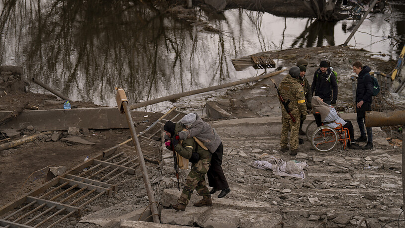 Ein ukrainischer Soldat trägt eine ältere Frau über einen Fluss bei Irpin am Stadtrand von Kiew. Foto: Emilio Morenatti/AP/dpa