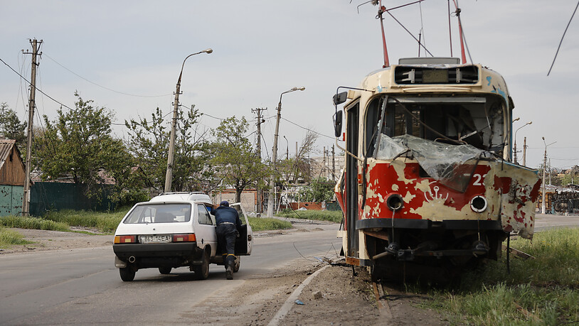 Ein Mann schiebt ein liegengebliebenes Auto an einer beschädigten Straßenbahn in Mariupol vorbei. Foto: Alexei Alexandrov/AP/dpa