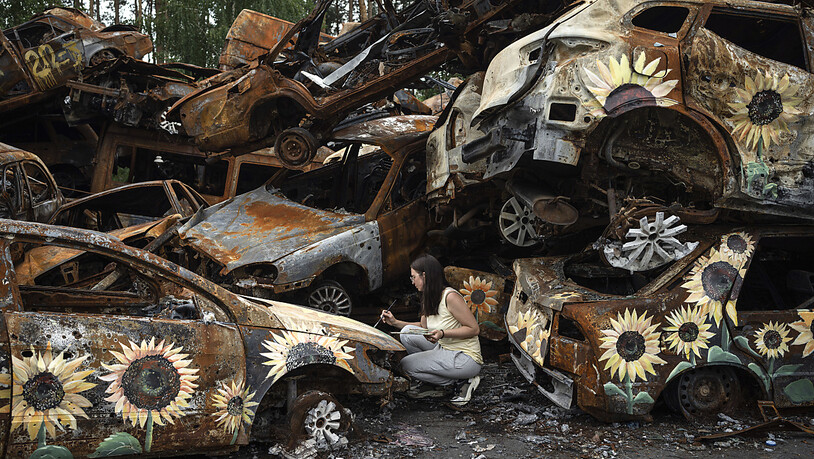 dpatopbilder - Olena Yanko, Künstlerin aus der Ukraine, malt Sonnenblumen auf Autos, die durch russische Angriffe zerstört wurden. Foto: Evgeniy Maloletka/AP/dpa