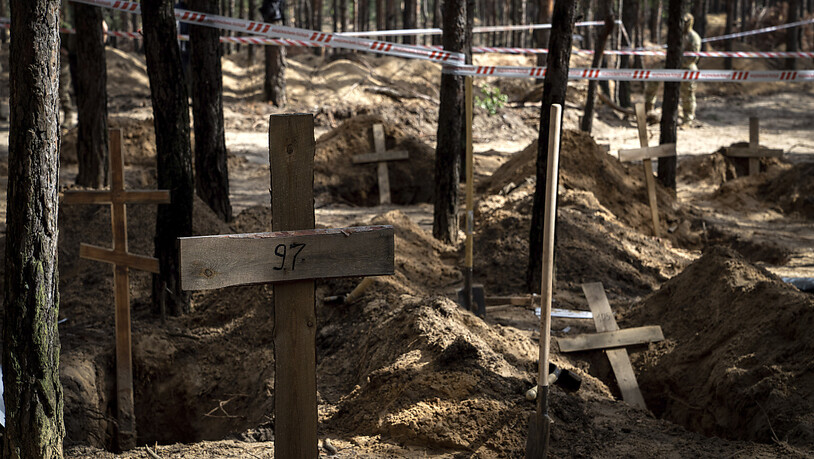 Ein Holzkreuz markiert ein nicht identifiziertes Grab während einer Exhumierung auf dem Waldfriedhof von Isjum. Foto: Evgeniy Maloletka/AP/dpa