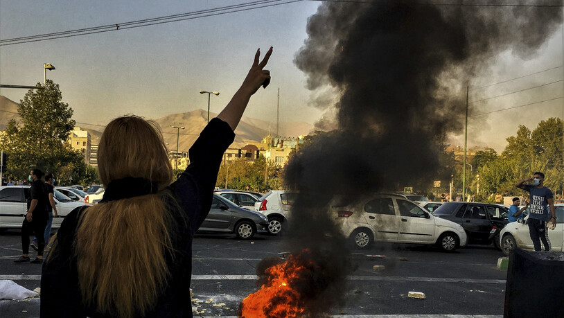 ARCHIV - Eine Frau steht in Teheran während einer Demonstration nach dem Tod der 22-jährigen Mahsa Amini vor einem brennenden Autoreifen und zeigt das Victory-Zeichen. Foto: Uncredited/AP/dpa