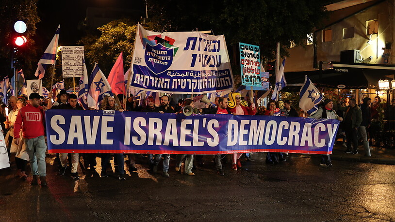 Menschen halten in Tel Aviv Banner und Plakate bei einem Protest gegen die neue rechte Regierung und die anstehenden Reformen. Foto: Ilia Yefimovich/dpa
