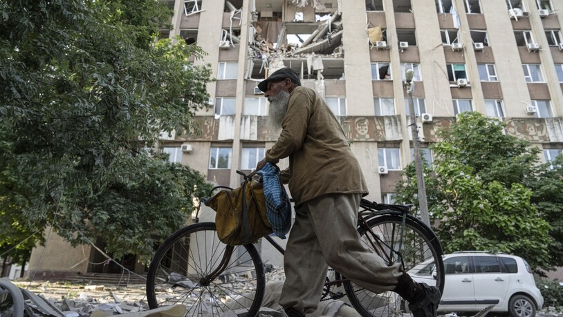Ein Mann in Cherson schiebt sein Fahrrad vor einem Gebäude entlang, das durch einen Luftangriff schwer beschädigt wurde. Foto: Evgeniy Maloletka/AP/dpa