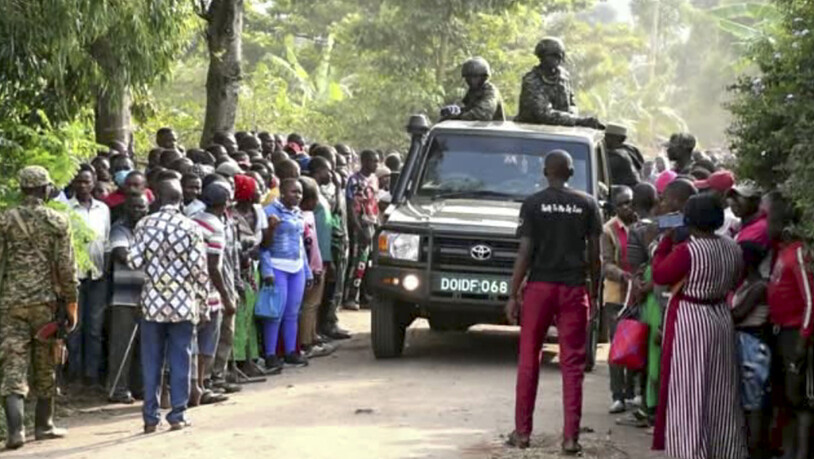 In diesem Videostandbild fahren Sicherheitskräfte an einer Menschenmenge vorbei, die sich nach einem Angriff auf die Lhubiriha Secondary School nahe der Grenze zum Kongo vor der Schule versammelt hat. Foto: Uncredited/AP/dpa