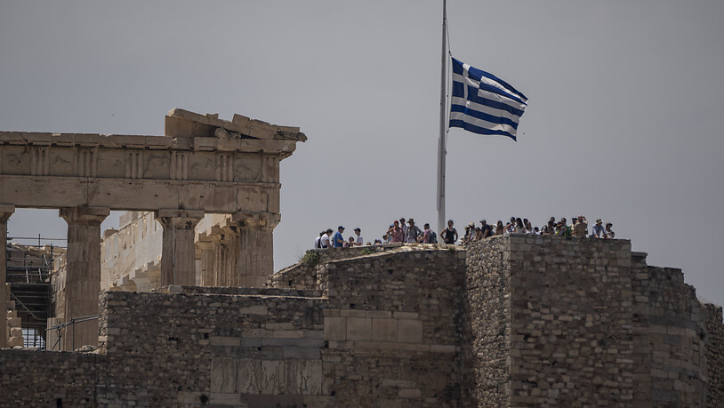 Die griechische Flagge weht auf Halbmast neben dem antiken Parthenon-Tempel, während Touristen den antiken Akropolis-Hügel besuchen. Foto: Petros Giannakouris/AP/dpa
