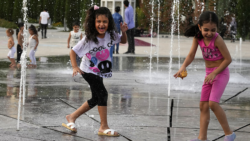 Kinder spielen am 1. August bei Temperaturen von rund 38 Grad Celsius unter einer Wasserfontäne im Ebrahim-Park. Foto: Vahid Salemi/AP/dpa