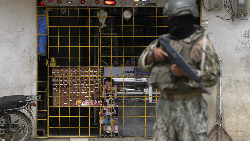 Ein Junge schaut hinter den Gitterstäben eines geöffneten Elektronikgeschäfts hervor, während ein Soldat an einem von der Armee eingerichteten Sicherheitskontrollpunkt Wache steht. Kurz vor der Präsidentenwahl in Ecuador ist ein weiterer Lokalpolitiker…