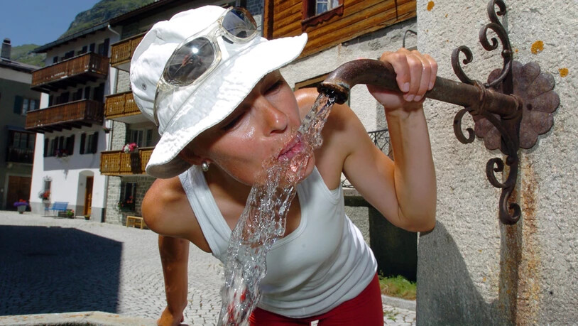 Eine Touristin trinkt Wasser aus einem Brunnen in Bivio.