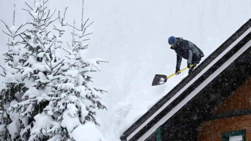 Ein Mann befreit ein Dach von der Schneelast am Mittwoch in der Nähe von Untertauern in Österreich.