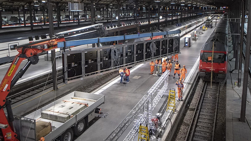Ein Kran hievt die Anzeigetafeln bei der Stirn des Luzerner Bahnhofs zur Montage in die Höhe.