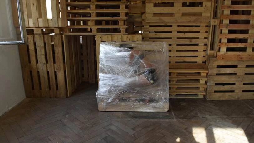 Ein fragiles, bewegliches Gut: Der vor dem Paletten-Haus verpackte Mensch löst viele Assoziationen aus. 