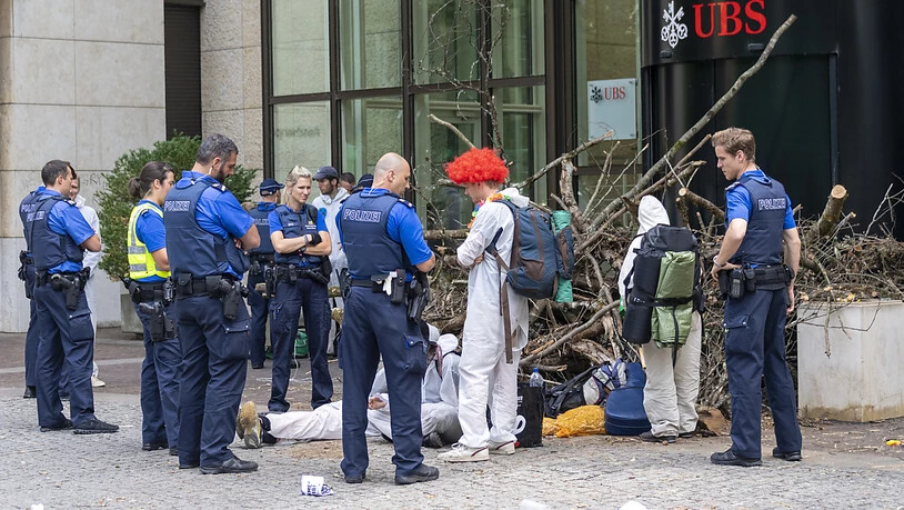 Polizisten räumten am Montag die Blockade der Aktivisten einer Gruppe namens "Collective Climate Justice" vor dem UBS-Bürogebäude am Aeschenplatz in Basel. Im Hintergrund eine Holzbeige, die an Schwemmholz erinnert, als Sperre vor der Türe. (Archivbild)