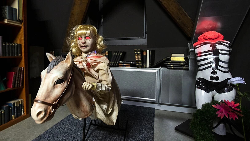 Eine gruselige Puppe wippt wortlos auf einem Schaukelpferd vor und zurück im neuen Geisterhaus des historischen Museums.