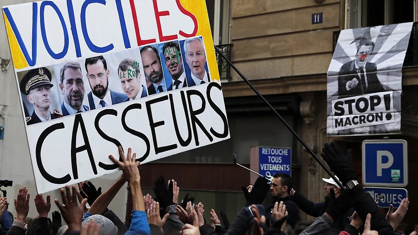 "Das sind die Unruhestifter", steht auf dem Plakat von Demonstranten in Paris mit den Fotos von Staatspräsident Macron, Regierungschef Edouard Philippe und weiterer Politiker.