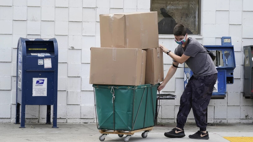 Ein Mann transportiert große Paketboxen. Foto: Damian Dovarganes/AP/dpa