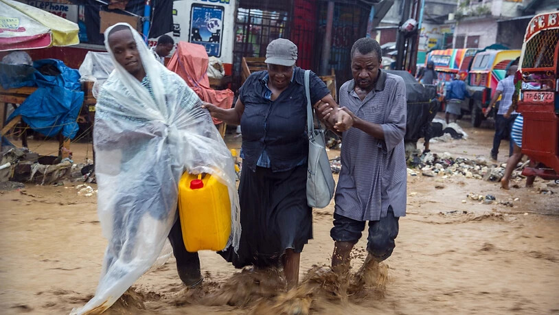 dpatopbilder - Menschen gehen während des Tropensturms «Laura» über eine überschwemmte Straße in Haitis Hauptstadt Port-au-Prince. Foto: Dieu Nalio Chery/AP/dpa