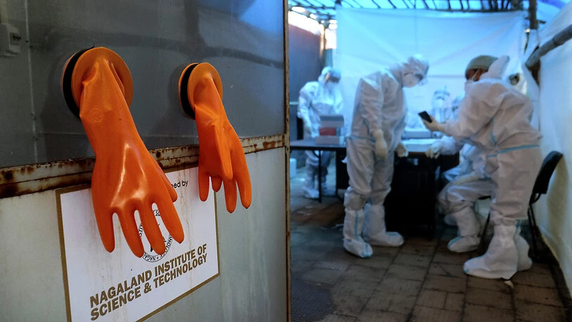 dpatopbilder - Ein Paar orangefarbener Schutzhandschuhe hängt aus einer Testkabine, während Mitarbeiter des Gesundheitswesens sich auf den Tag in einem COVID-19-Testzentrum des nordöstlichen indischen Bundesstaates Nagaland vorbereiten. Foto: Yirmiyan…