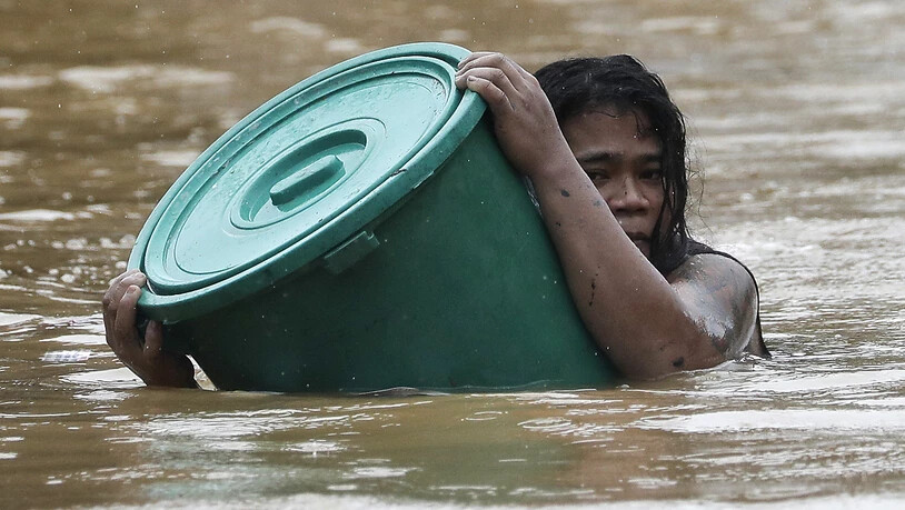 Eine Anwohnerin hält sich an einen Plastikbehälter als Schwimmboje fest, während sie in dem steigenden Hochwasser schwimmt. Foto: Aaron Favila/AP/dpa