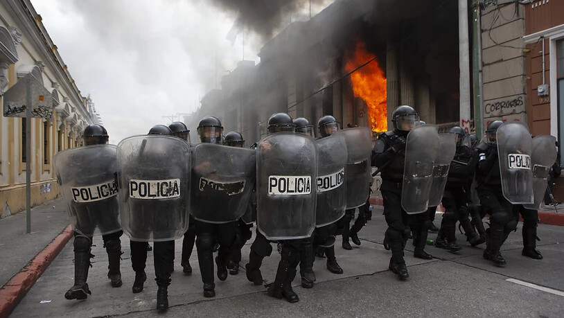 Polizisten bilden eine Blockade gegen Demonstranten. Bei Protesten gegen den Haushalt 2021 haben Demonstranten Teile des Kongresses in Brand gesteckt. Foto: Oliver De Ros/AP/dpa