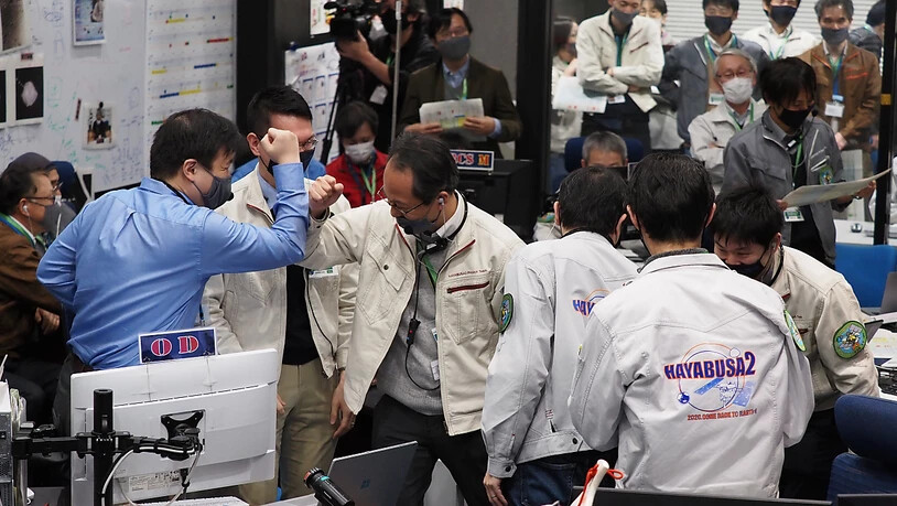 HANDOUT - Die Projektteilnehmer jubeln in einem Kontrollraum des JAXA-Campus Sagamihara, nachdem die erfolgreiche Trennung einer Kapsel vom Raumschiff Hayabusa2 bestätigt wurde. Foto: -/JAXA/AP/dpa