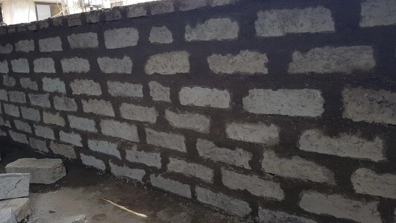 HANDOUT - Eine Mauer aus Bausteinen, die je zur Hälfte aus desinfizierten und geschredderten Masken und Schutzanzügen sowie aus einer Abfallmasse, die bei der Papierproduktion entsteht, und einem Bindemittel bestehen (undatierte Aufnahme). Foto: -/Binish…