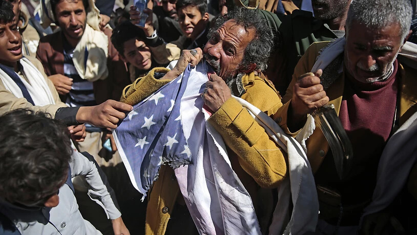 ARCHIV - Ein Anhänger der jemenitischen Huthi-Bewegung zerreißt während eines Protest vor der geschlossenen US-Botschaft eine US-Fahne, nachdem US-Außenminister Pompeo angekündigt hat, die Huthi-Rebellen als Terrororganisation einzustufen. Foto: Hani…