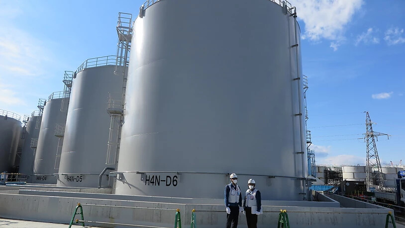 ARCHIV - Zwei Mitarbeiter des Betreiberkonzerns Tepco stehen vor riesigen Tanks, in denen verstrahltes Wasser, das bei der andauernden Kühlung der beschädigten Reaktoren von Fukushima anfällt, gelagert wird. Foto: Lars Nicolaysen/dpa