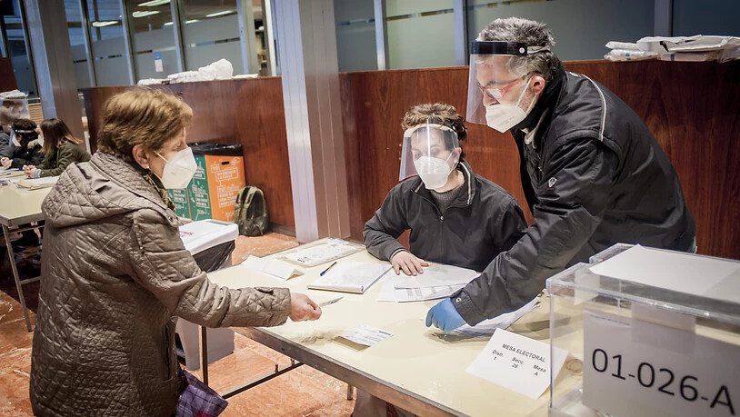 Wahlhelfer kontrollieren unter Beachtung der Corona-Maßnahmen die Dokumente einer Frau, bevor sie ihre Stimme für die katalanischen Regionalwahlen abgibt. Foto: Jordi Boixareu/ZUMA Wire/dpa