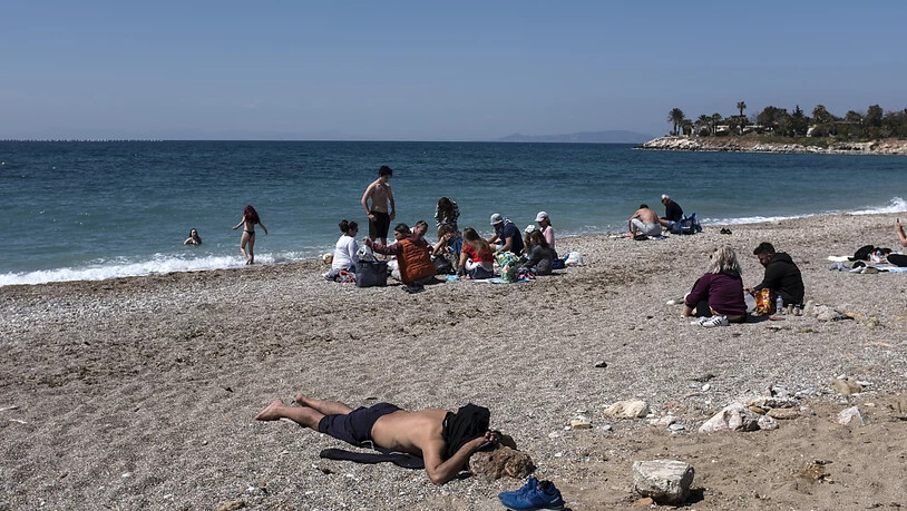 Menschen genießen einen sonnigen Tag an einem Strand im Athener Vorort Glyfada. Foto: Yorgos Karahalis/AP/dpa