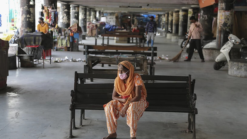 Eine Frau trägt eine Schutzmaske und wartet an einem verlassenen Busbahnhof. (Archivbild) Foto: Channi Anand/AP/dpa