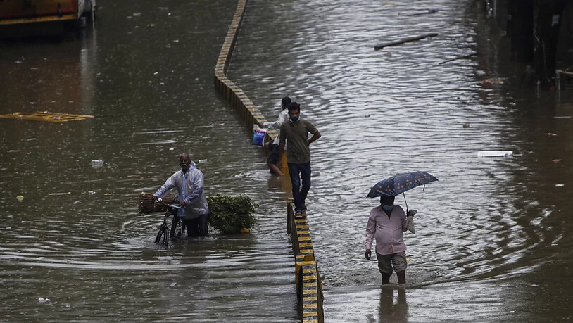 Menschen bahnen sich in Mumbai ihren Weg durch eine überschwemmte Straße nach starken Regenfällen. Foto: Rajanish Kakade/AP/dpa