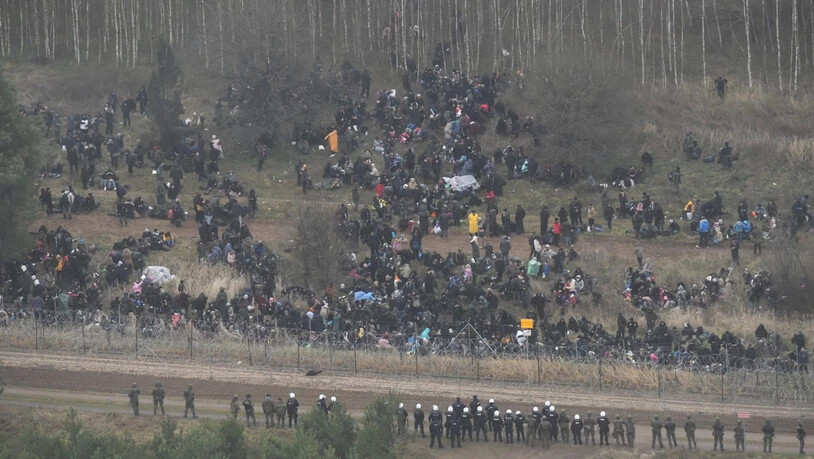 HANDOUT - Menschen stehen hinter einem Grenzzaun in Belarus in der Nähe des polnisch-belarussischen Grenzübergangs. Die Europäische Union wirft dem Machthaber von Belarus, Alexander Lukaschenko, vor, in organisierter Form Menschen aus Krisenregionen wie…