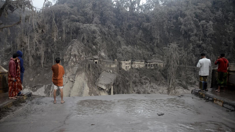 Dorfbewohner stehen vor einem Hang an der eine Brücke durch den Lavastrom, bei Ausbruch des Mount Semeru, zerstört wurde. Foto: Hendra Permana/AP/dpa