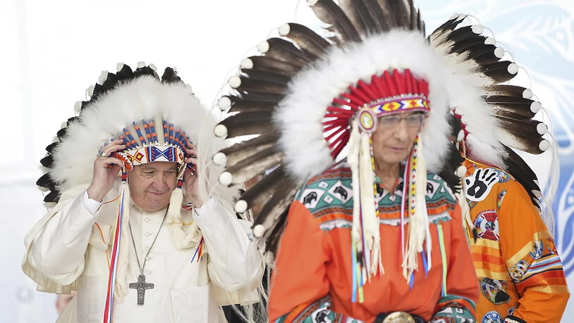 Papst Franziskus (l) rückt einen traditionellen Kopfschmuck zurecht, der ihm während einer Zeremonie überreicht wurde. Foto: Nathan Denette/The Canadian Press/AP/dpa