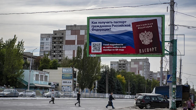 Menschen überqueren eine Straße mit einem Plakat mit der Aufschrift "Wie man den Pass eines russischen Bürgers bekommt" vor dem Scheinreferendum in der von den Russen kontrollierten Volksrepublik Luhansk. Foto: Uncredited/AP/dpa