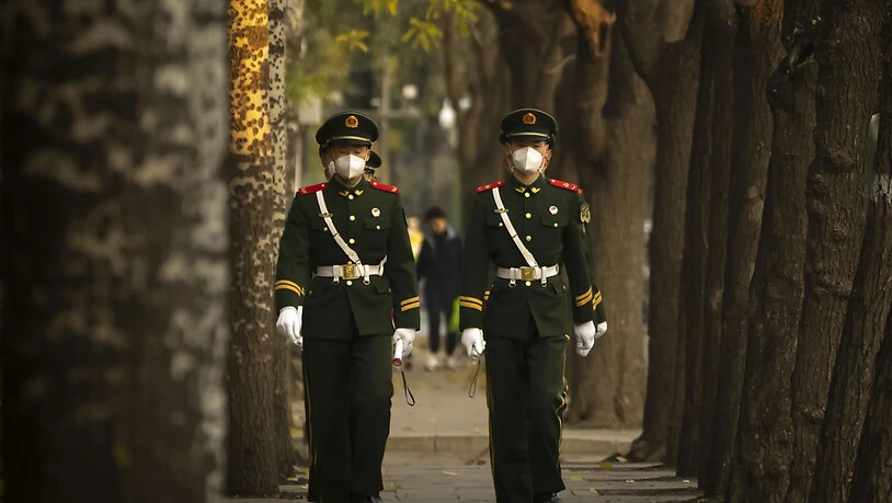 Chinesische paramilitärische Polizisten mit medizinischen Masken gehen eine Straße in Peking entlang. Foto: Mark Schiefelbein/AP/dpa